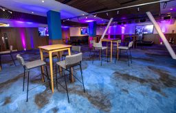 purple and pink lights, modern event space, high tables and chairs, plasma screen, lecturn, stage