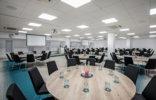 cabaret layout, water glasses, water bottles, two projector screens, black chairs and white walls