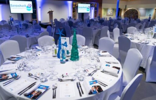 cabaret layout, conference, two TV screens, numbers on tables, Seashell brochures, water bottles, lecturn, stage
