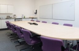 modern meeting room, conference call device on table, purple chairs, kitchenette to the side of the room