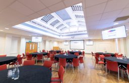 cabaret layout, projector screen, plasma screens, water bottles and glasses, red chairs and black covered tables