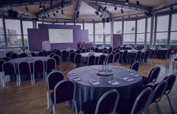 conference setup, projector screen, head table on stage, cabaret layout, notepads ontables, water and glasses