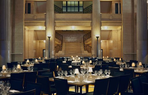 litly dim room, large venue space, square tables with wine and water glasses, grand staircase, event space